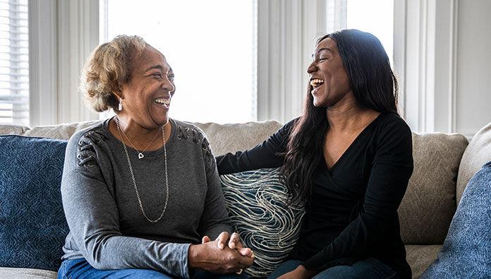 Mom and her daughter laughing while sitting on a couch Mom and her daughter laughing while sitting on a couch
